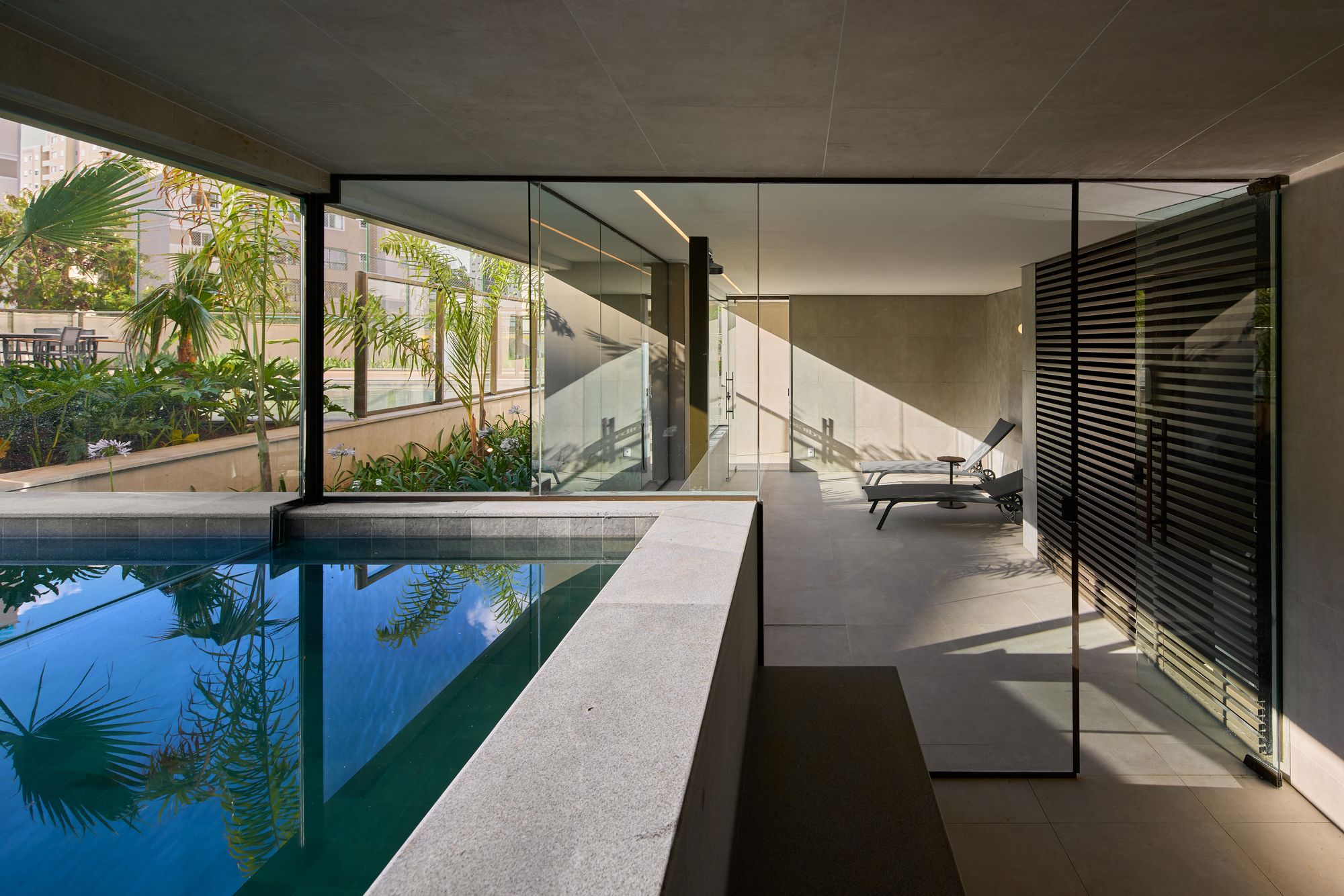Piscina com borda de vidro e paisagismo em áreas comuns